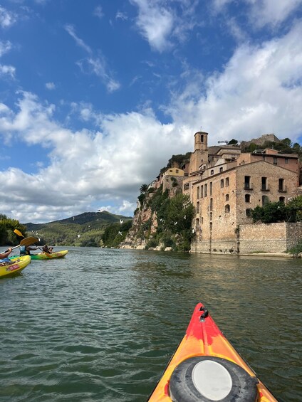 A river with kayaks, a historic building on a cliff, and a clear sky. 1