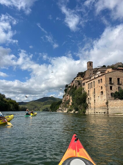 A river with kayaks, a historic building, and a mountainous landscape. 3