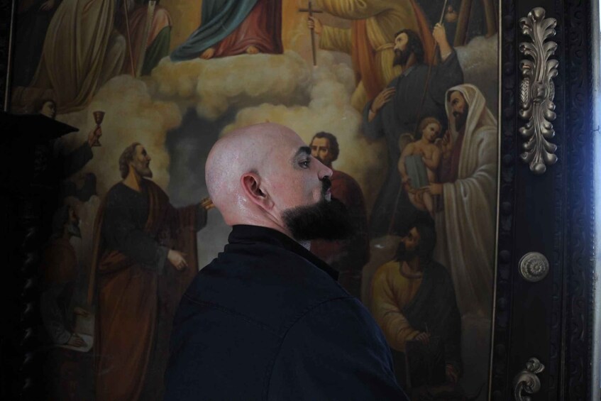 Eine Person steht vor einem religiösen Gemälde mit Figuren und Wolken. 2