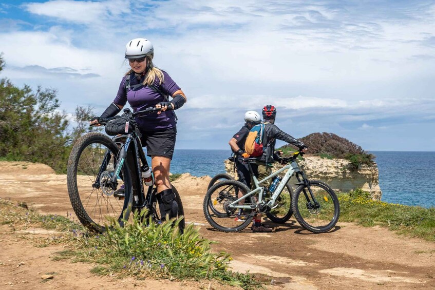 Two cyclists on a dirt path with a coastal landscape in the background. 3