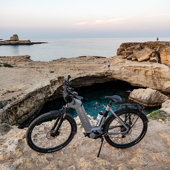 A mountain bike parked on rocky terrain near a coastal cliff with people in the background. 4