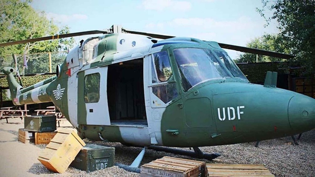 A military helicopter with the letters 'UDF' on its nose, parked outdoors with crates and equipment around it. 3