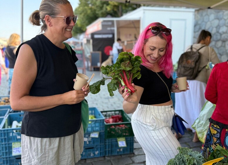 Deux personnes tenant des légumes-feuilles et des gobelets en papier dans un marché en plein air. 1