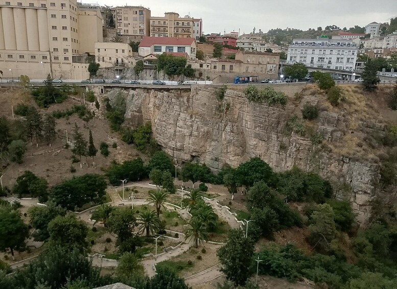A cityscape with a prominent cliff, buildings, and a road with vehicles. 3