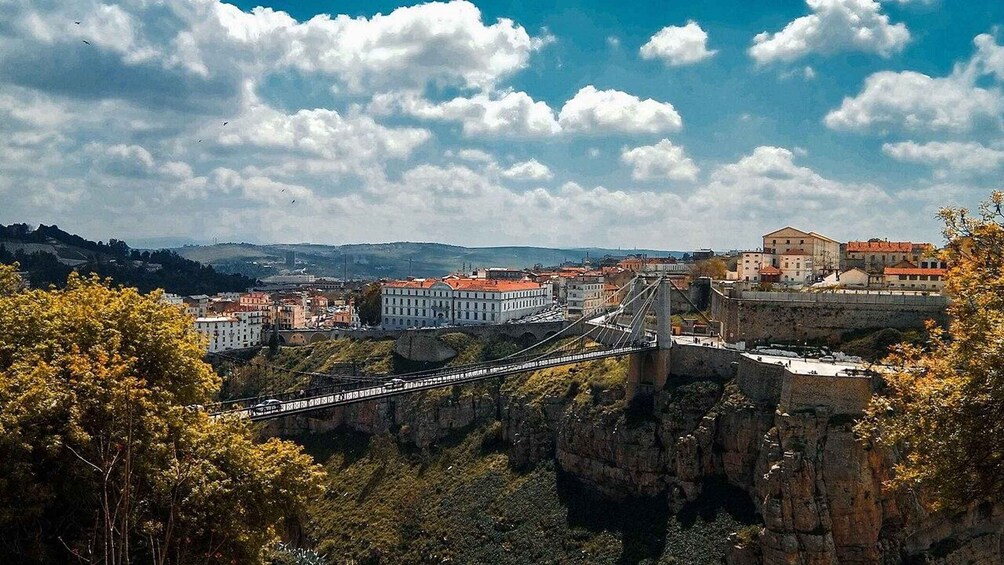 A cityscape with a prominent bridge spanning a deep gorge, surrounded by buildings and greenery. 1