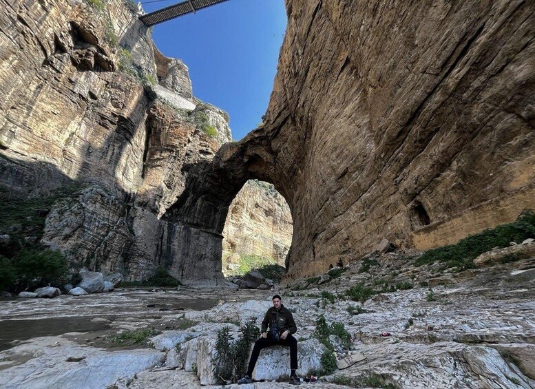 A person sitting on a rock in a canyon with a large rock arch formation. 4