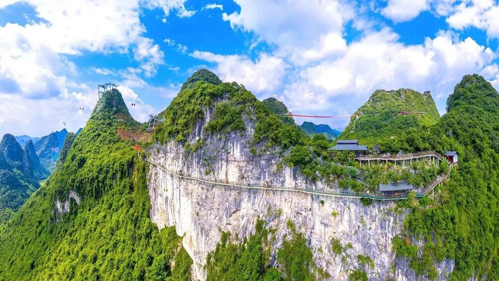 Un pont suspendu enjambant une falaise, avec une végétation luxuriante et des bâtiments traditionnels. 1