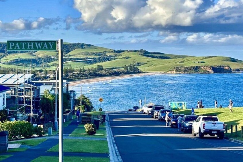 A coastal road with a sign reading 'PATHWAY,' parked cars, and a beach in the background. 2