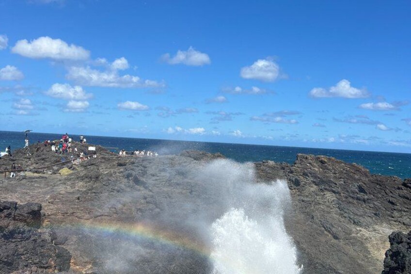 A rocky coastline with a rainbow, ocean waves, and people observing the scenery. 4