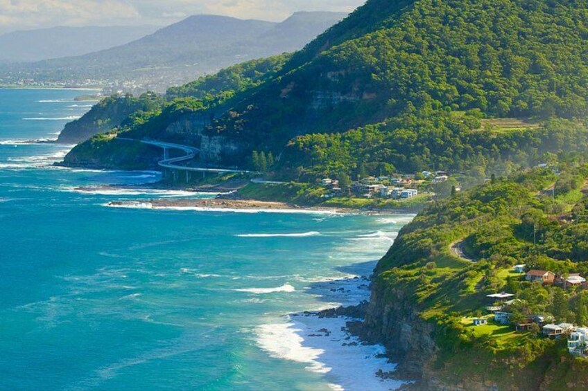 A coastal landscape with a winding road, a bridge, and houses on a hillside. 5