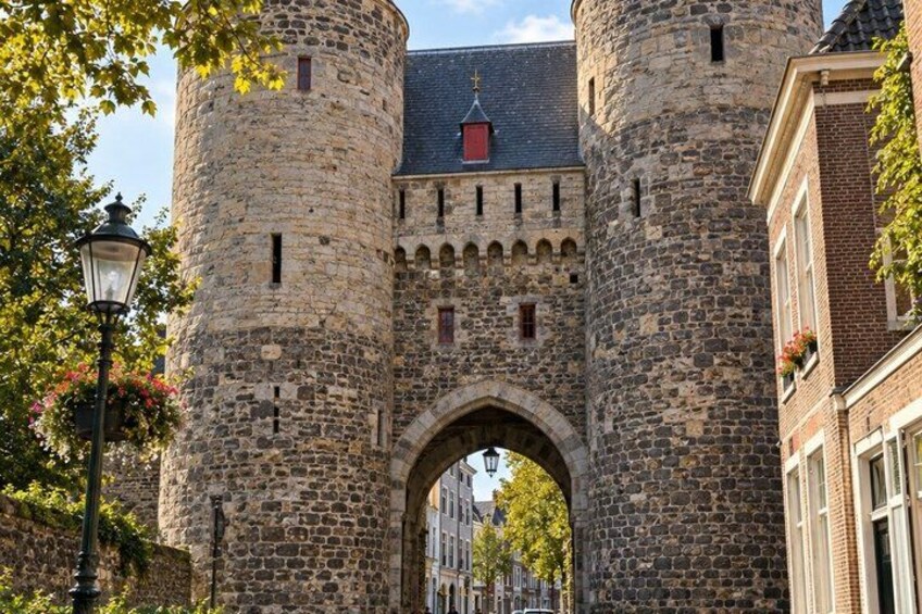 A historic stone gate with a central archway, flanked by two cylindrical towers, and a street lamp to the left. 2