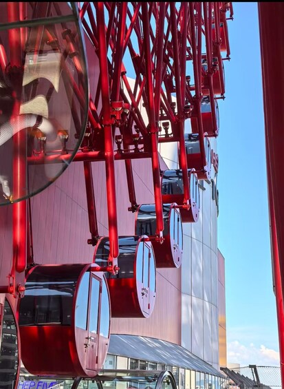 Un réseau de téléphériques rouges, composé de plusieurs cabines suspendues à un ensemble de câbles rouges, se déploie devant un bâtiment moderne. 1