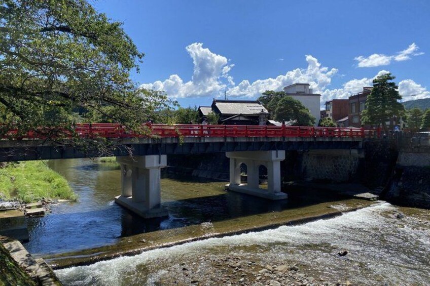 A bridge with a red railing, a river below, and buildings in the background. 3
