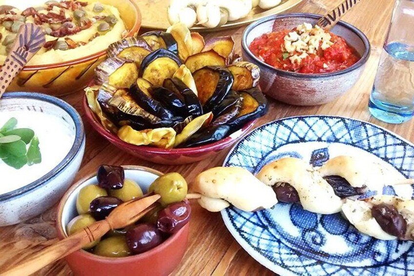 A table with various dishes including a bowl of olives, a plate of pastries, and a bowl of tomato-based food. 5