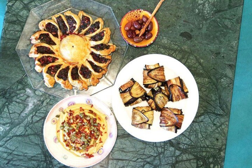A round pastry on a plate, a bowl of olives, and a plate of sliced vegetables. 4
