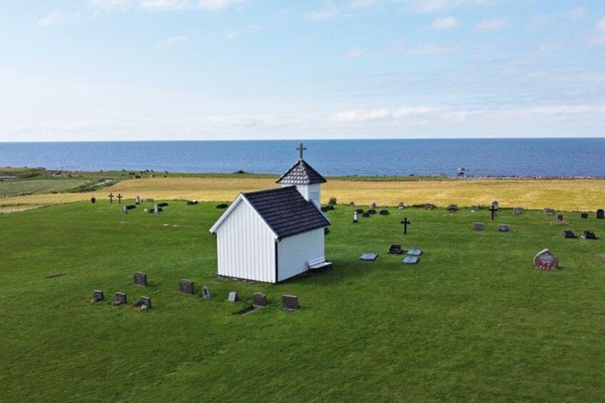 A small white church with a steeple, surrounded by a grassy cemetery with headstones, near a body of water. 4