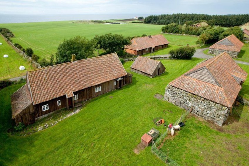 A rural farm with several wooden and stone buildings, a green field, and a sheep. 3