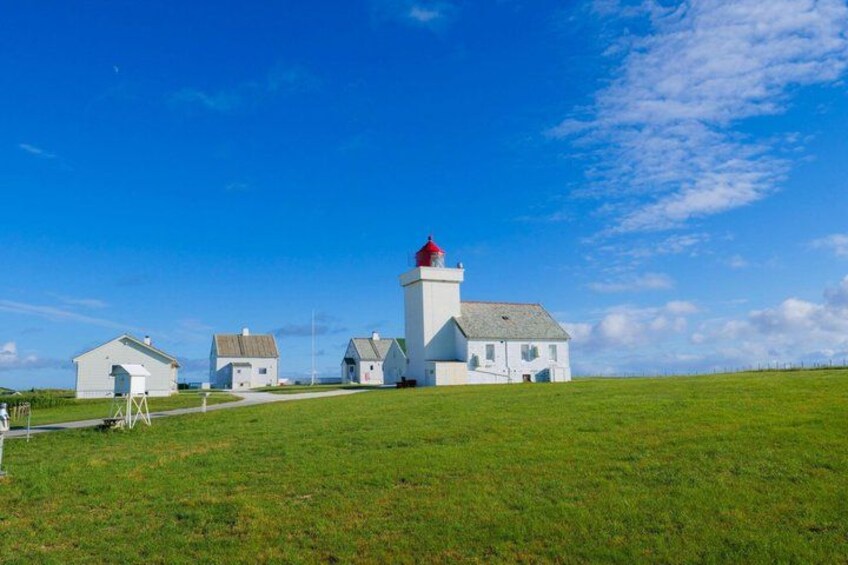 A coastal lighthouse with a red top, surrounded by white buildings on a grassy hill under a clear blue sky. 2