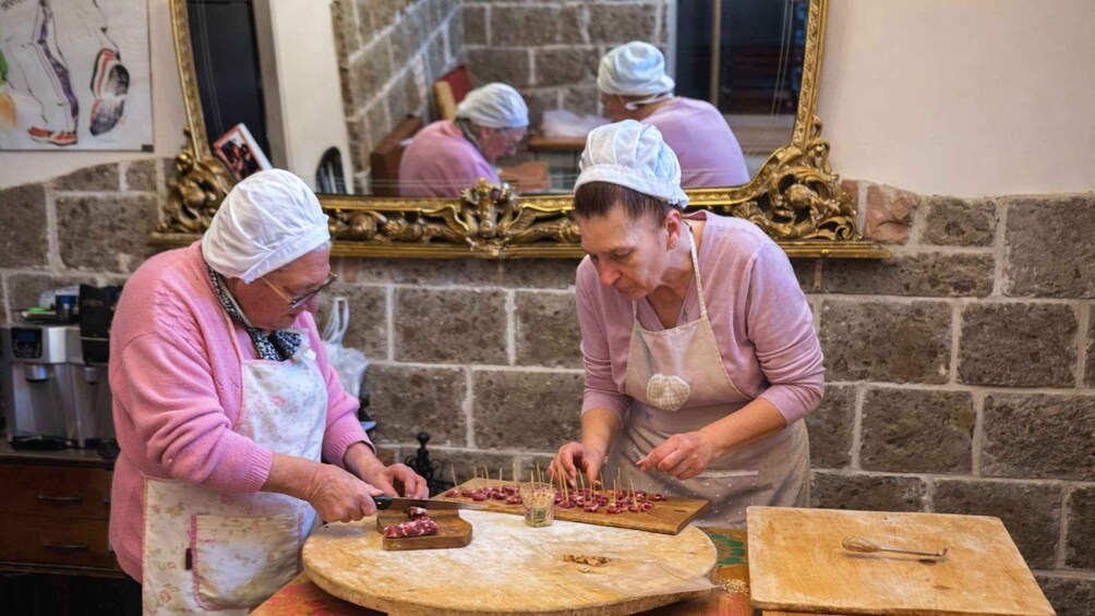 Two individuals preparing food, one slicing meat and the other arranging skewers on a board. 2