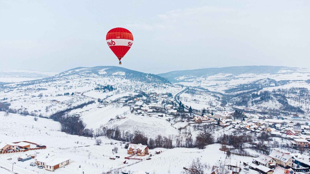 Eine verschneite Landschaft mit einem roten Heißluftballon am Himmel. 5