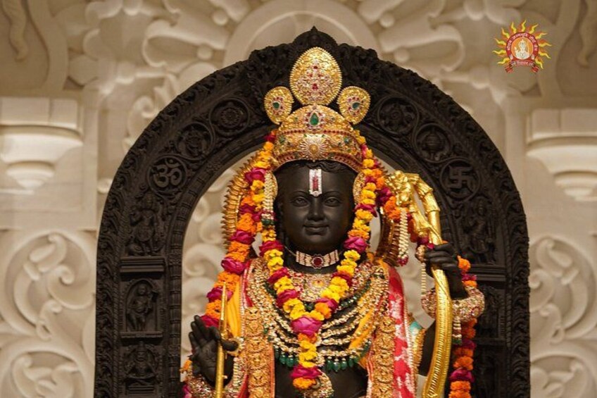 A statue of a deity adorned with garlands and jewelry, set against an ornate architectural backdrop. 1