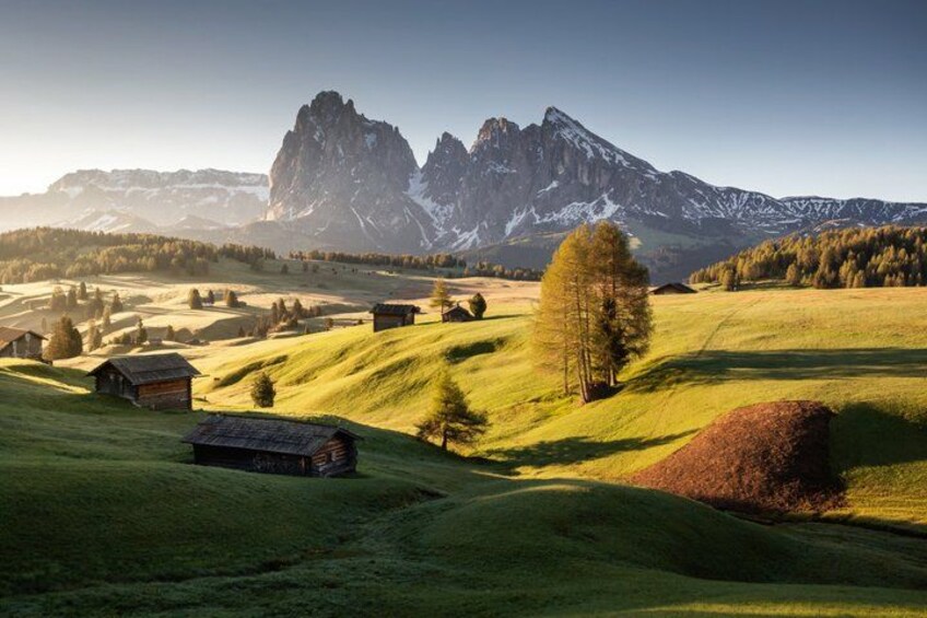 A mountainous landscape with rolling green hills, scattered houses, and a prominent tree. 1
