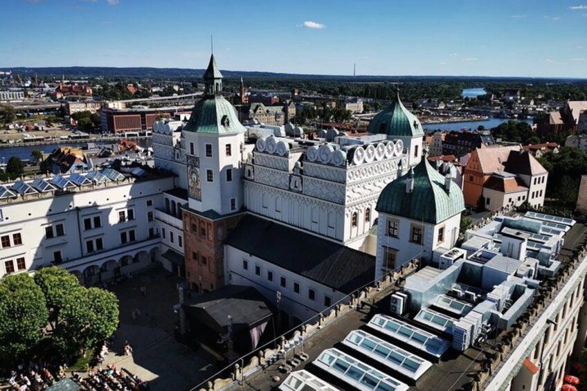 A large historic building with multiple domes and a central tower, surrounded by a parking lot and a river in the background. 2