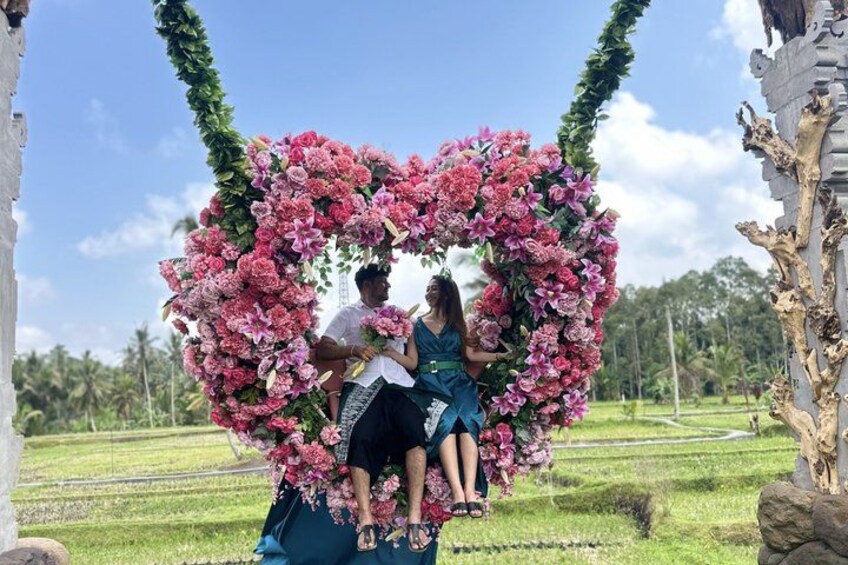 A heart-shaped floral arch with people sitting on a swing. 4
