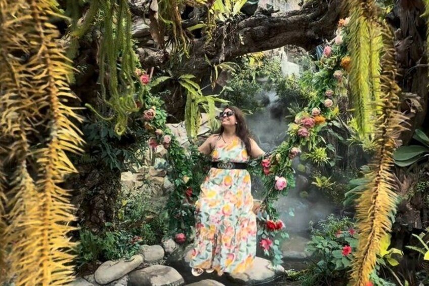 A woman in a floral dress standing in a lush garden with a variety of plants and flowers. 5