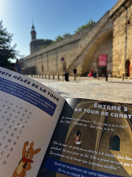 Un livre comportant du texte et une illustration de lapin, posé sur un mur de pierre avec une tour en arrière-plan. 3