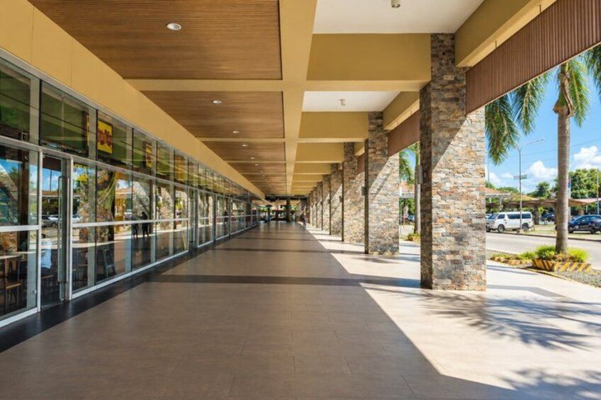 A covered walkway with glass windows, stone pillars, and a paved path. 1