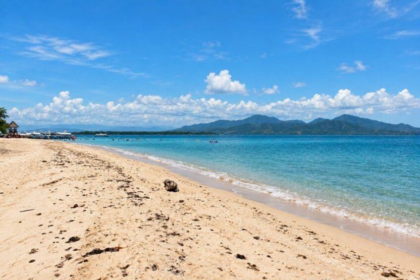 A sandy beach with clear turquoise water, a few footprints, and mountains in the distance. 4