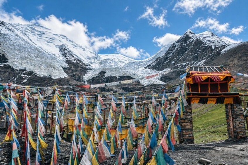 A mountainous landscape with snow-capped peaks, a stone structure, and colorful prayer flags. 2