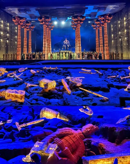 A stage with a group of people in traditional costumes, a large illuminated sculpture, and a backdrop with vertical columns. 3