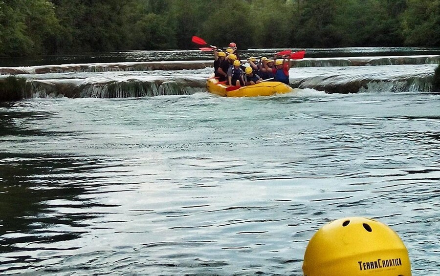 Eine Gruppe von Menschen in einem gelben Schlauchboot, das einen Fluss mit einem Wasserfall befährt. 4
