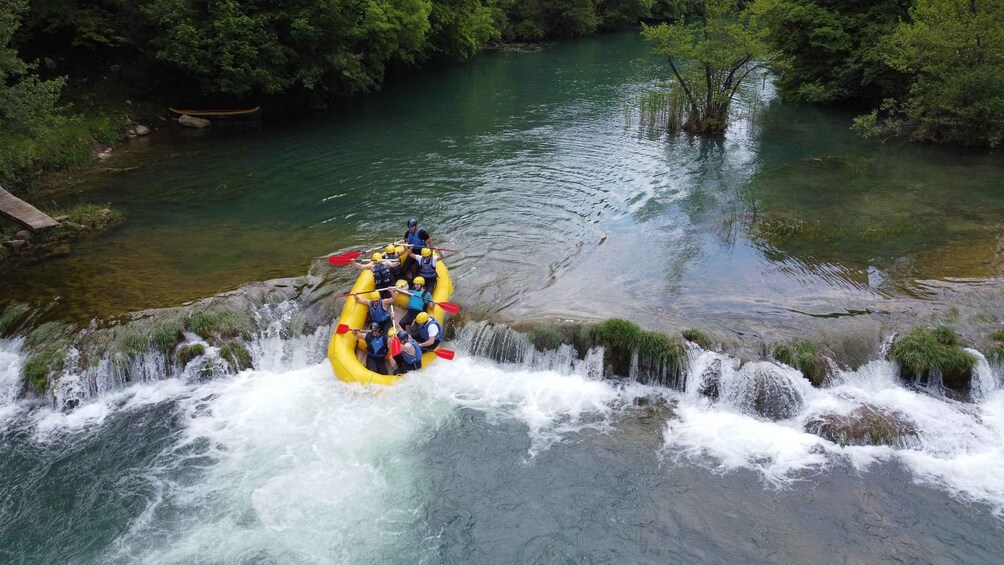 Eine Gruppe von Personen in einem gelben Floß, das einen Fluss mit einem Wasserfall befährt. 2