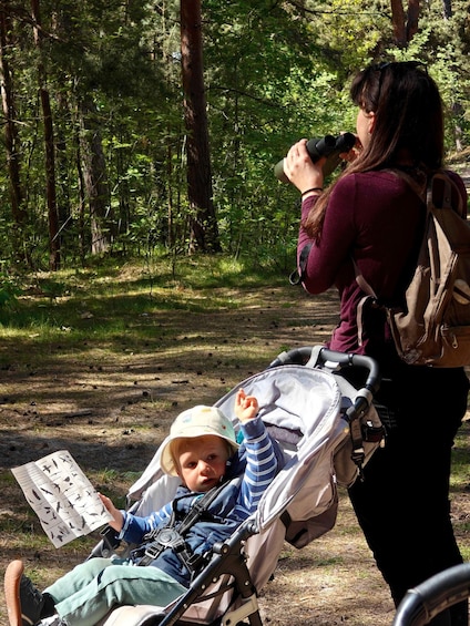 Eine Person im Wald mit Fernglas, und eine andere Person mit Kinderwagen. 5