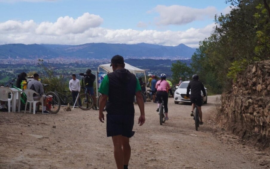 A dirt path with people walking and cycling, a tent, and a view of distant mountains and a city. 4