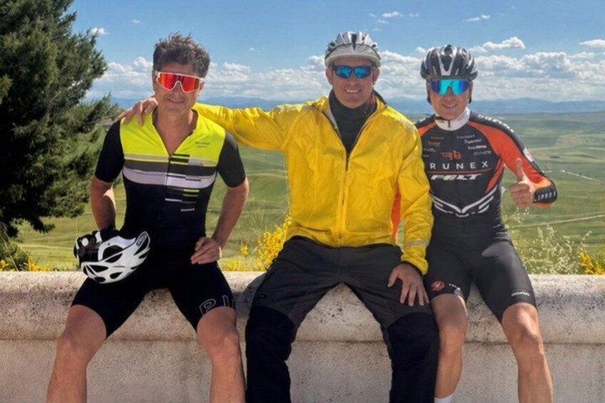 Three cyclists on a ledge with a scenic view of a valley. 2