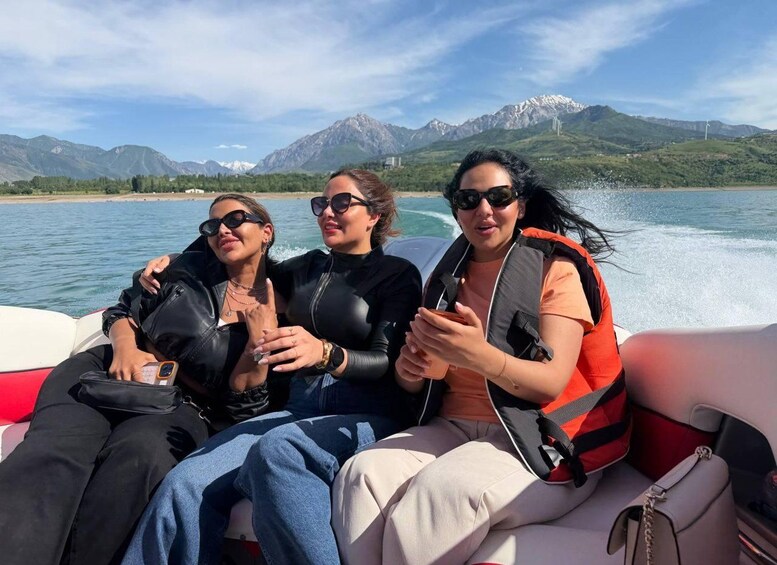 Trois personnes se trouvent sur un bateau, avec un paysage montagneux en arrière-plan. 1