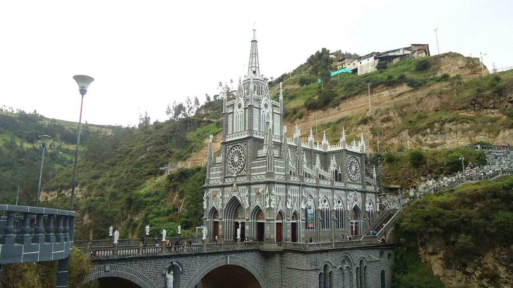 Une église de style gothique, dotée d’une architecture complexe, un pont orné de statues et une colline parsemée de bâtiments. 3