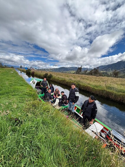 Un groupe de personnes se trouve à bord d’un petit bateau sur une rivière, entouré de rives verdoyantes et de montagnes lointaines. 4
