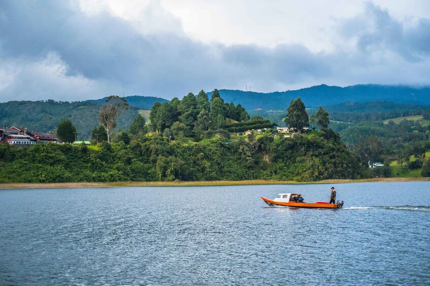 Un petit bateau orange sur un lac paisible, avec une colline boisée en arrière-plan. 2
