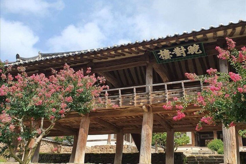 A traditional wooden structure with a sign, surrounded by blooming pink flowers. 3