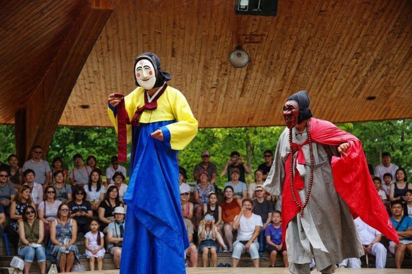 Two performers in traditional costumes on a stage with an audience. 5