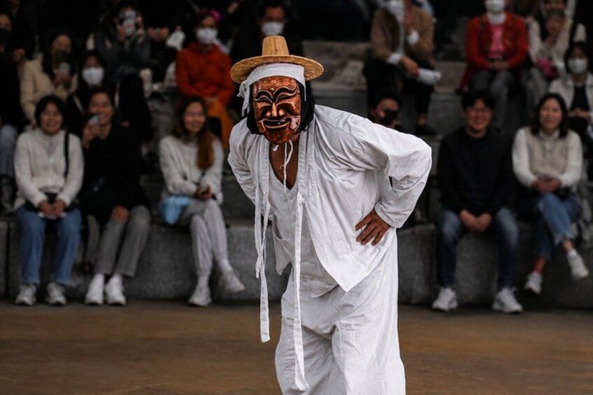 A person in a white outfit and straw hat performing in front of an audience. 1