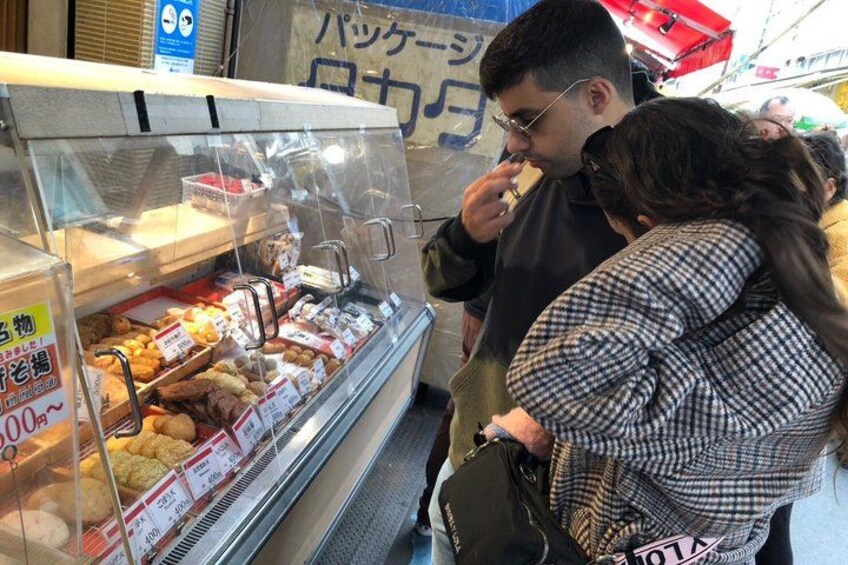 A person eating from a food stall with a glass display case. 3