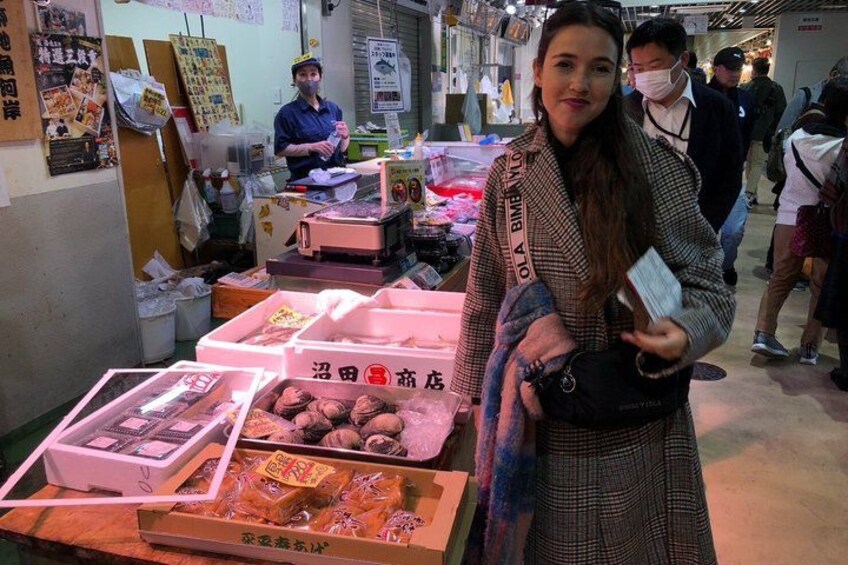 A person standing at a market stall with various food items displayed. 4