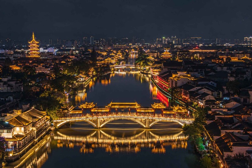 Une vue nocturne d’une ville historique, avec ses ponts illuminés, son architecture traditionnelle et une rivière qui reflète les lumières. 1