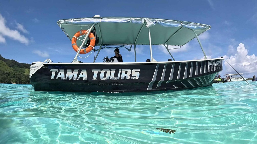 A boat named 'TAMA TOURS' with a canopy and an orange life buoy on clear turquoise water. 5